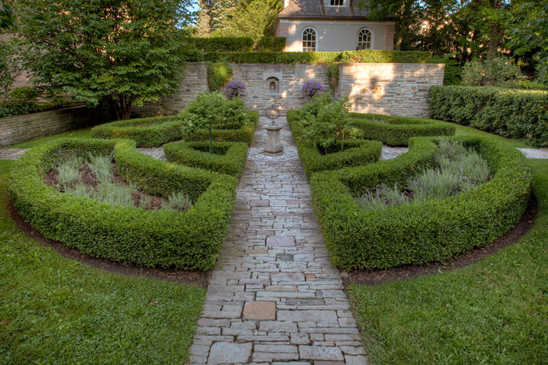 a round hedge with statue in the middle and stone path